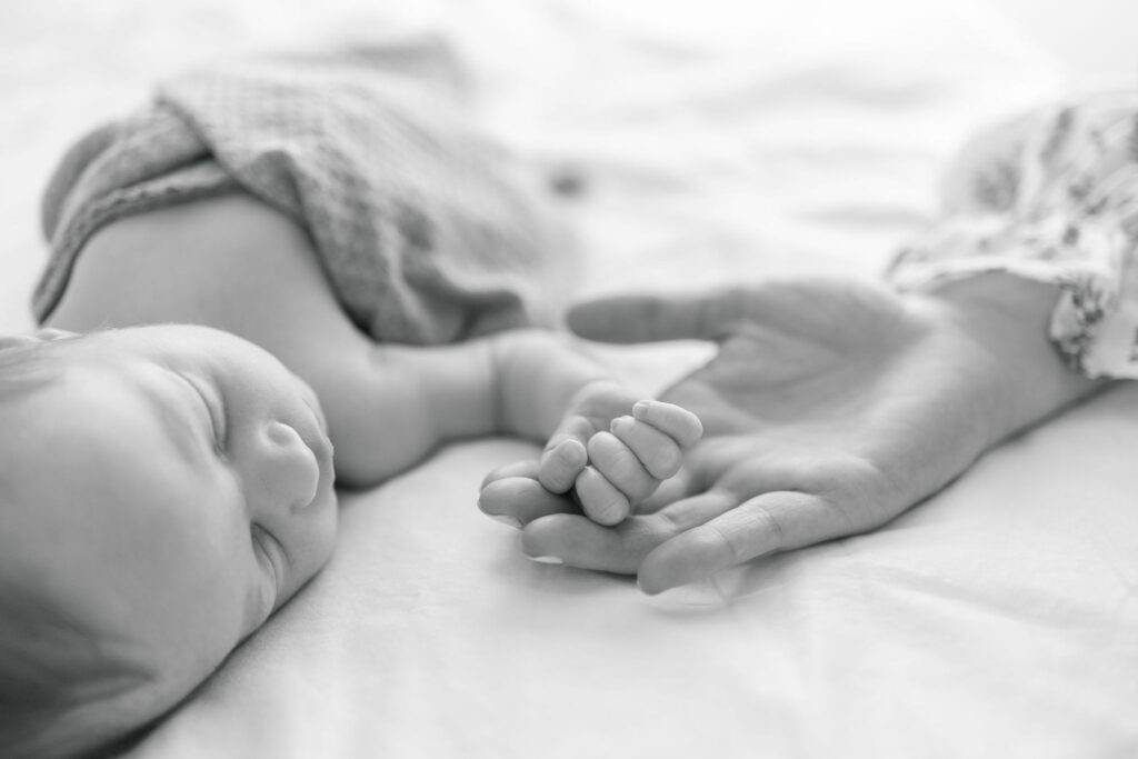 Sleeping baby's hand rests in mother's hand. 