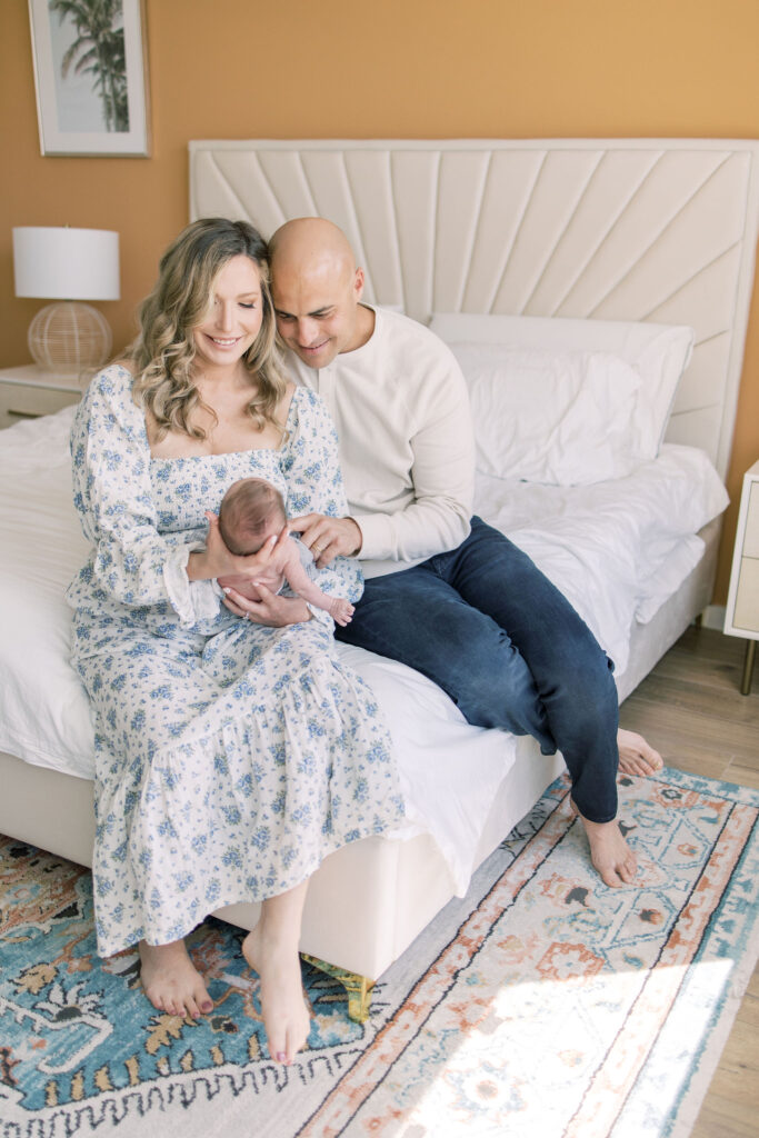 Couple sit on the edge of their bed admiring their newborn. 
