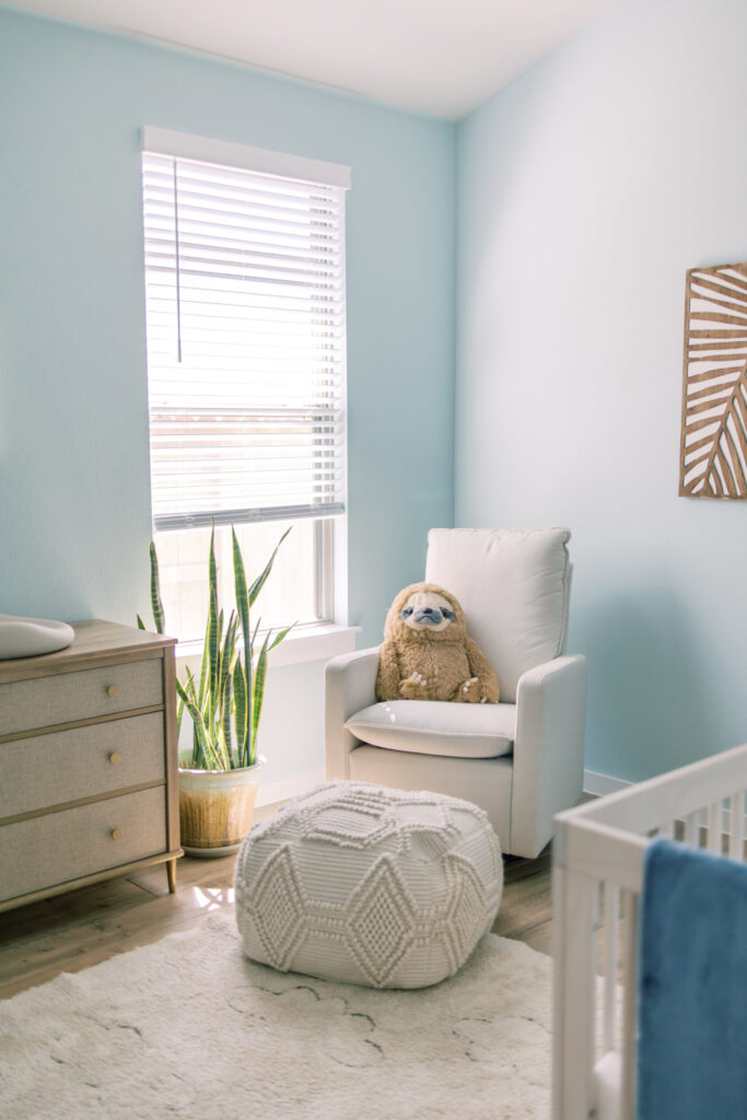 Baby blue nursery with sloth stuffed animal in rocking chair.