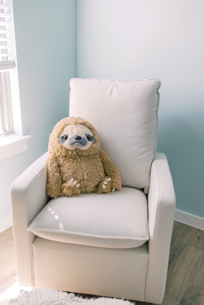 Large stuffed animal sloth sits in beige rocking chair.