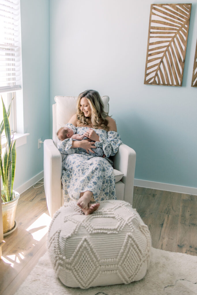 Mom smiles at newborn as she holds him in nursery rocking chair.