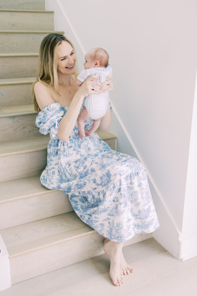 Mom holds baby boy up to her face and smiles at him as she sits on the stairs during a newborn session.